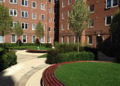 Thumbnail 1 of 8 - a courtyard with grass and trees in front of a brick building