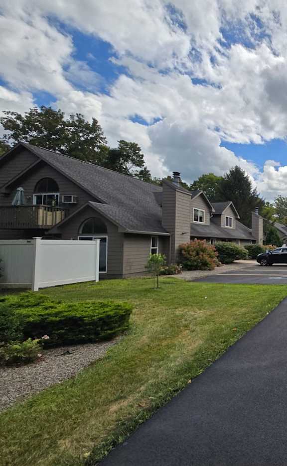 A residential street with houses on both sides and cars parked on the right side.