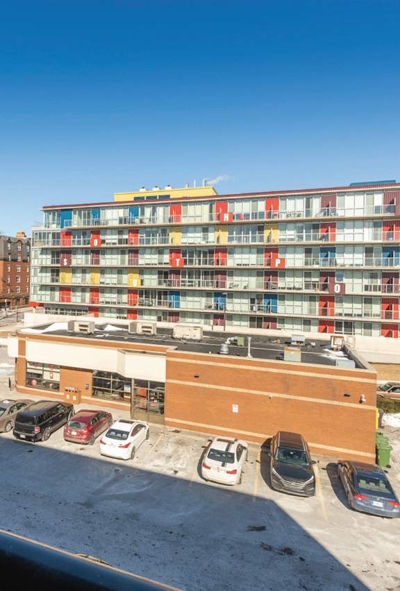 A parking lot with cars and a multi-story building with red and yellow balconies.