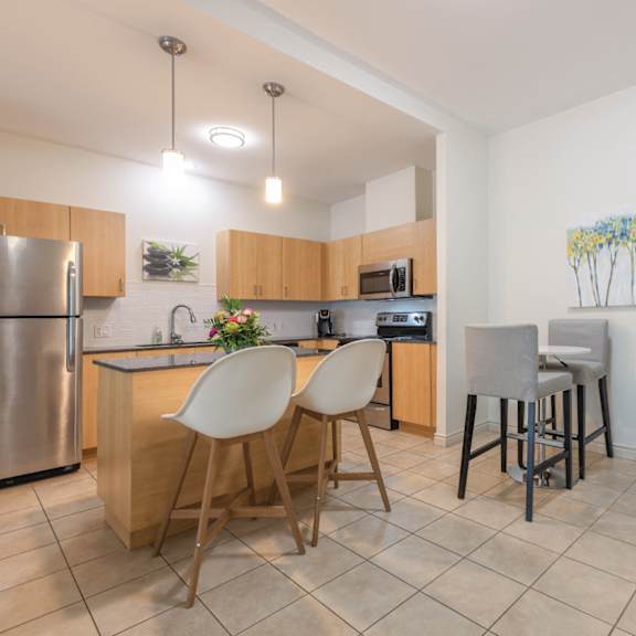 A kitchen with a refrigerator, microwave, and bar stools.
