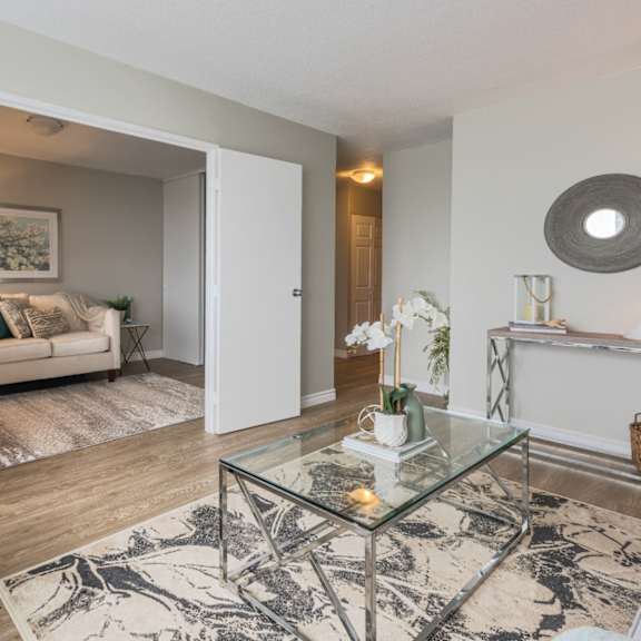 A living room with a glass coffee table and a grey couch.