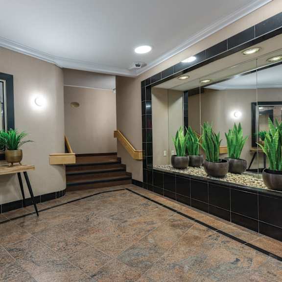 A hallway with a mirror, potted plants, and a bench.