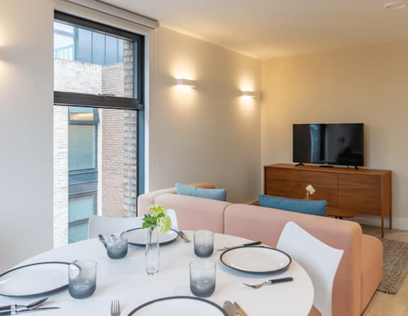 A dining table set with plates and glasses is in front of a couch and a television.
