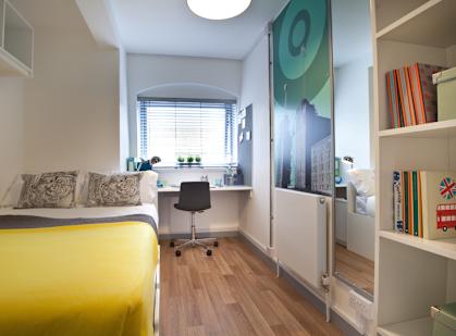 a bedroom with a yellow bed and a desk and a window