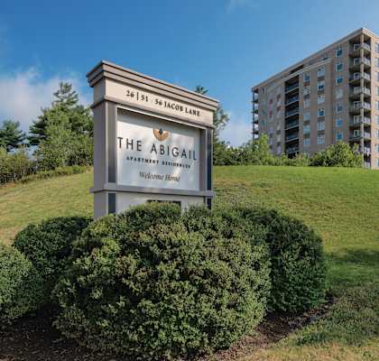 A sign for The Abigail Apartment Residence stands in front of a large building.