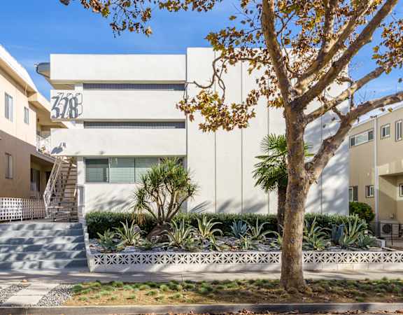 a white apartment building with a tree and plants in front of it