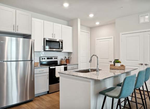 A modern kitchen with a stainless steel refrigerator, microwave, and a sink with a countertop and chairs.