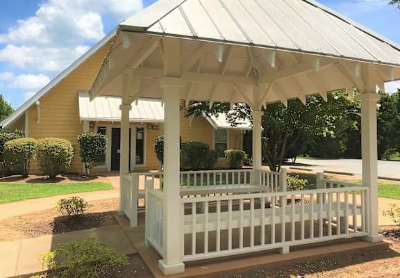A white gazebo is in front of a yellow house.