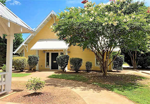 A yellow house with a white porch and a tree in front.