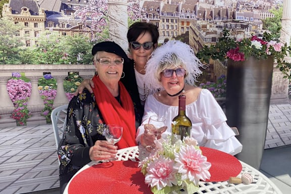 Three women are sitting at a table with wine glasses in front of a scenic city view.