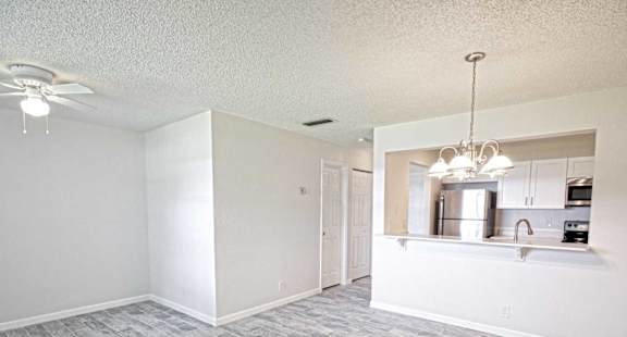 an empty living room with a kitchen and a ceiling fan