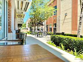 An outdoor dining area with chairs and tables in front of a local business near trees and bushes at the Tioga Town Center.