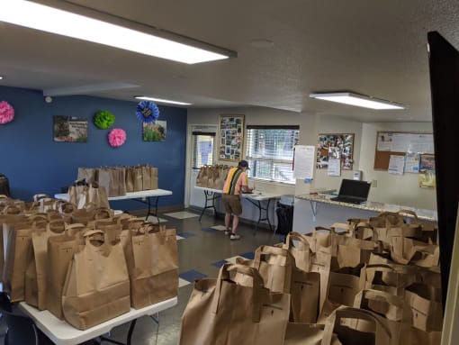 Grocery Bags sit on folding tables in the River Garden community room