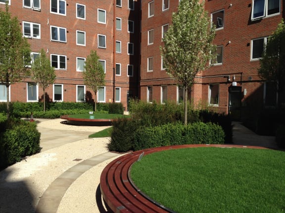 a courtyard with grass and trees in front of a brick building