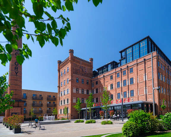A large brick building with a tower and a smaller modern building in front of it.