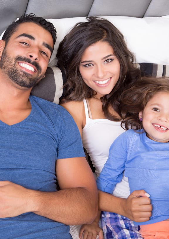 A family of three is sitting closely together on a couch.