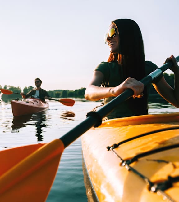 A woman in a kayak wearing sunglasses paddles through the water.