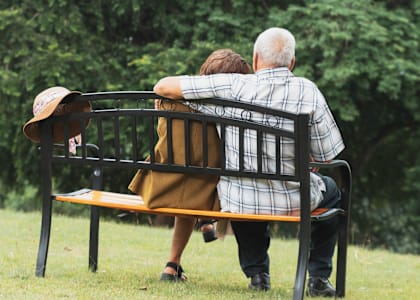 An elderly couple is sitting on a bench in a park.
