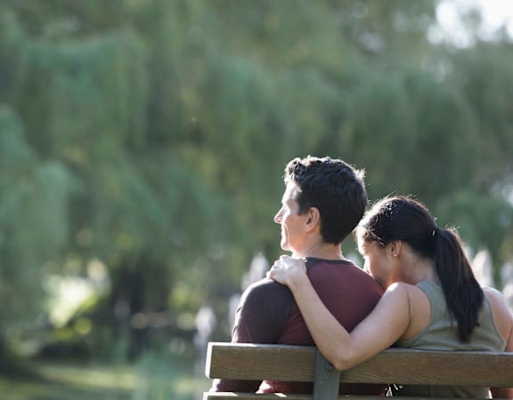 A couple is sitting on a bench in a park.