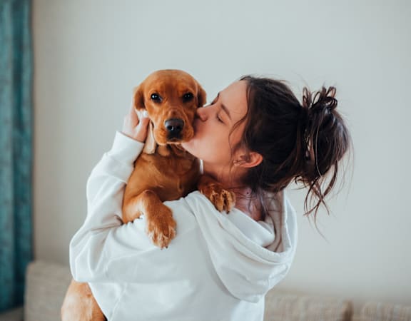 A woman in a white shirt is holding a brown dog.