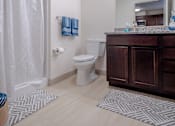 Thumbnail 7 of 9 - Bathroom of an apartment with vinyl flooring, a high ceiling, a vanity, a wide mirror, and excellent lighting.