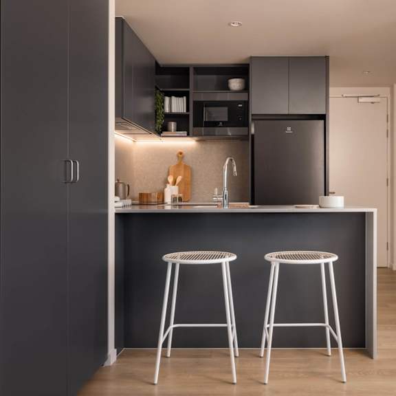 A kitchen with a black fridge, white stools and a grey backsplash.