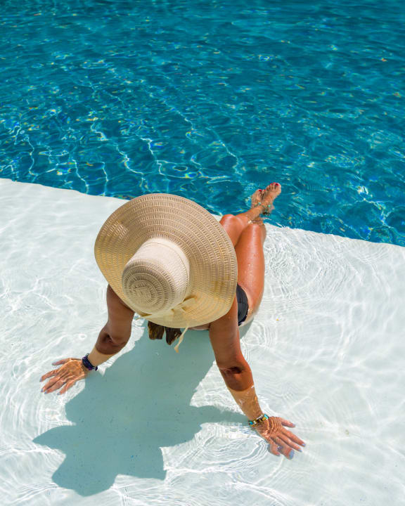 a woman laying in a pool with a floppy hat