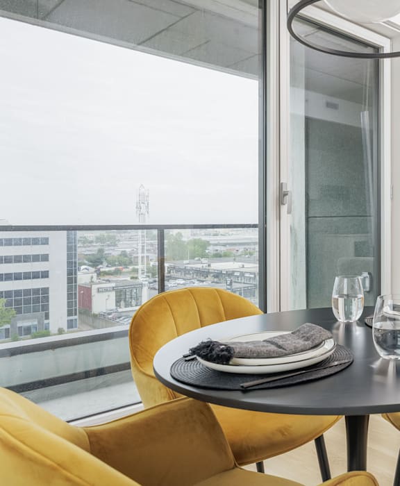 A table with a plate and glasses on it with a chair and a window in the background.
