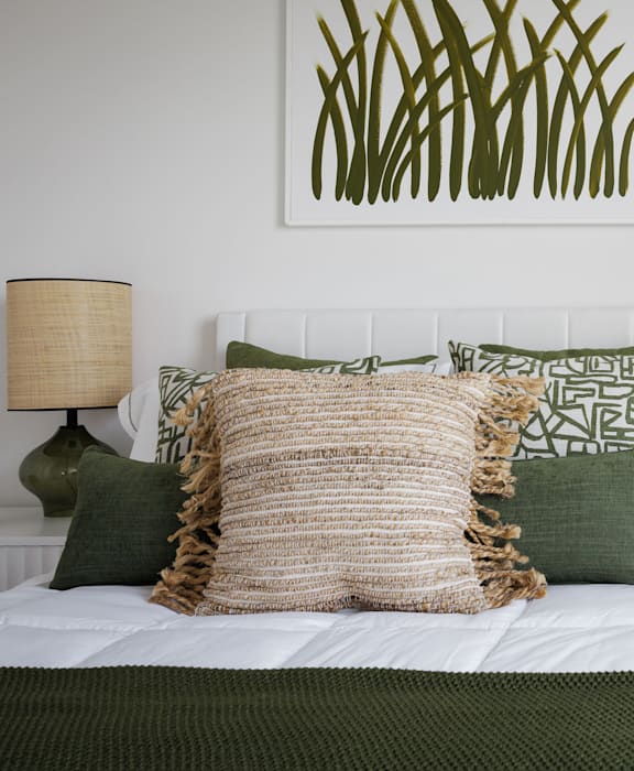 A bed with a white headboard and a green throw on it.