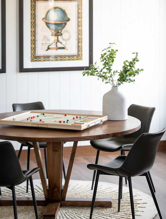 A table with a vase, chair and a book on it.