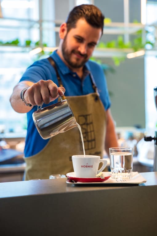 a man in a blue shirt and apron pouring coffee into a cup