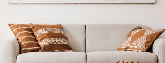 Banner Image-  The clubhouse is furnished with two cream colored sofas, an oversized tan chair, a blue chair, and a dining room table with three chairs positioned around it.