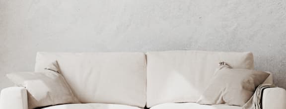 a white chair with white pillows and a white lamp in a room with a white wall