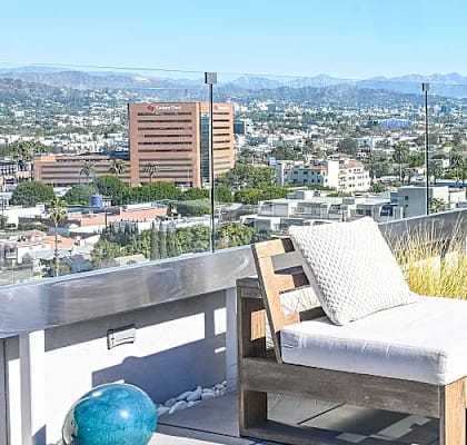 A patio with a couch, chairs, and a table overlooking a city.