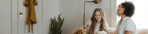 Two women sitting on a couch with a dog between them.