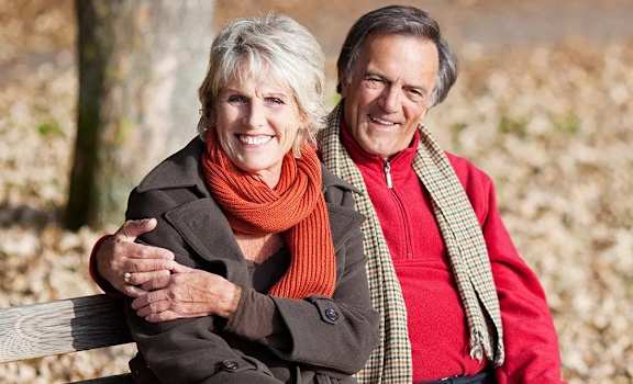 An older couple is sitting on a bench in a park.