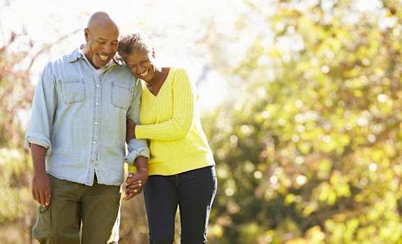 A couple walking hand in hand in a sunny outdoor setting.