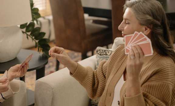 two older women sitting on a couch talking and playing cards