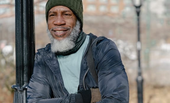 an older man wearing winter clothes and smiling and leaning against a light pole