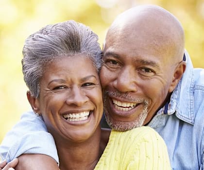 An older couple is smiling and embracing each other in a park.