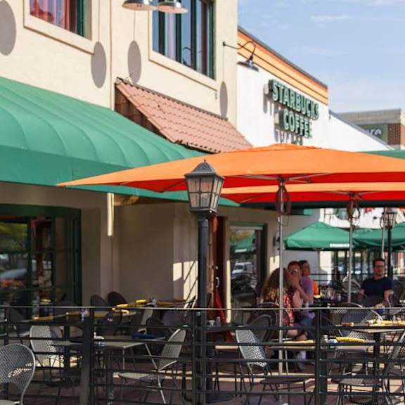 A row of outdoor tables are set up under umbrellas on a sidewalk.