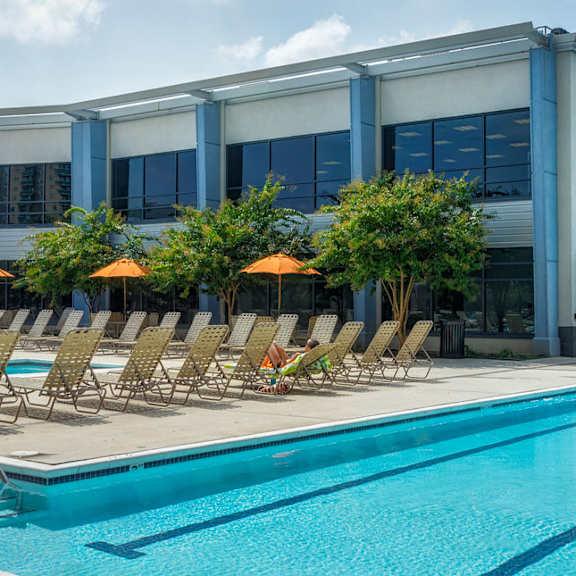 A large swimming pool with lounge chairs and umbrellas in front of a modern building.