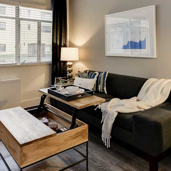 A living room with a couch, a chair, a coffee table, and a window with blinds.