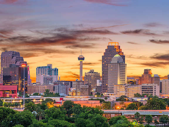 A city skyline at sunset with a mix of modern and older buildings.