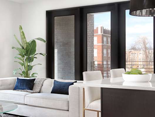 A modern living room with a white couch and a glass coffee table. at The Elle on Lockwood Apartments, Webster Groves, MO, 63119