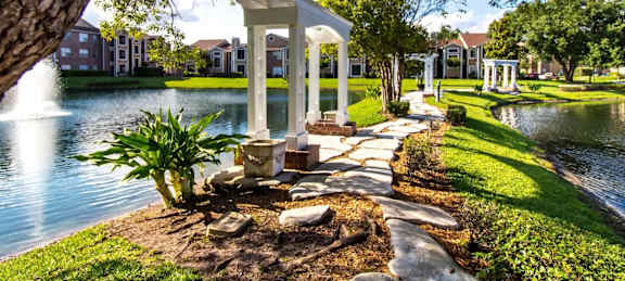 A gazebo is situated in a garden by a pond.