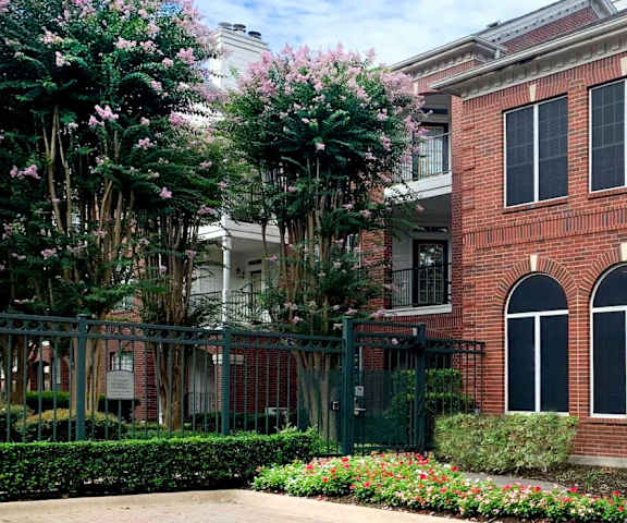 A red brick building with a black gate and a green bush.