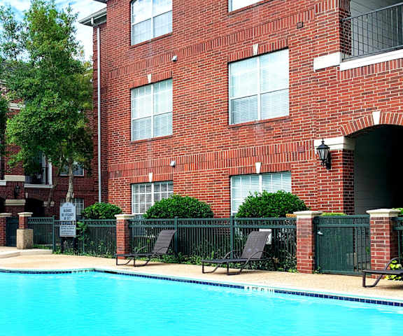 A pool surrounded by a brick building and trees.
