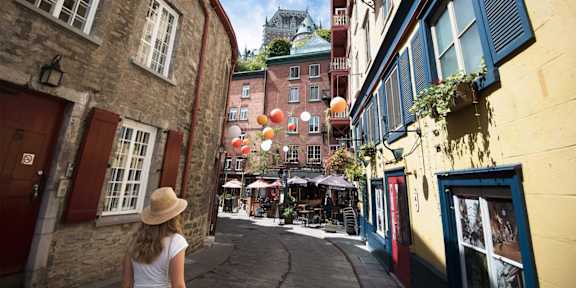 a woman walking down a street with buildings and balloons
