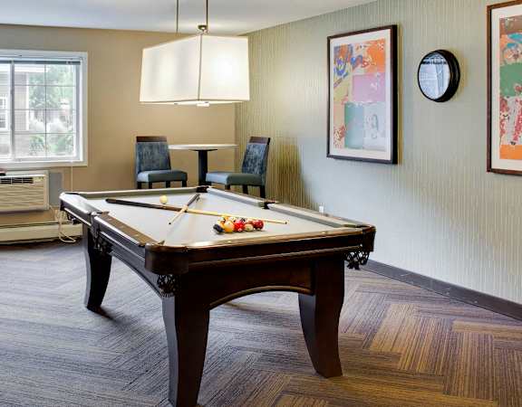 A pool table is in the middle of a room with a window and a chair.